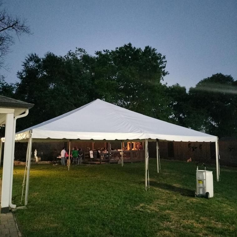 A frame tent glowing at dusk in a Houston back yard